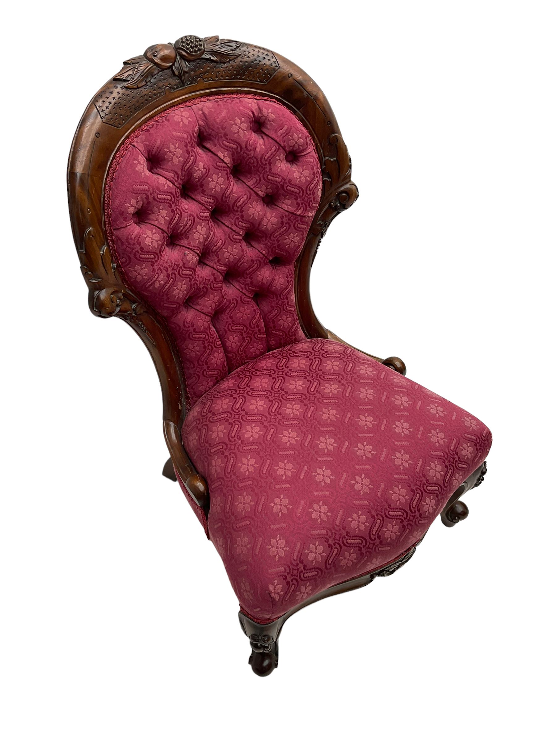 Victorian style mahogany framed nursing chair, the cresting rail carved with fruit and foliage, upholstered in red patterned fabric with buttoned back, on cabriole supports with scrolled terminals