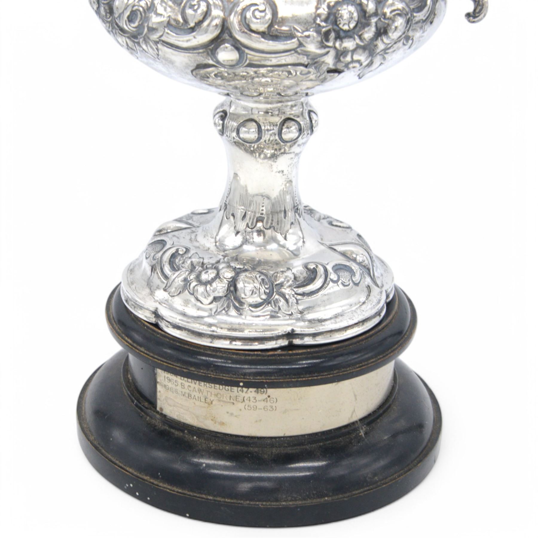 Victorian silver twin handled trophy, the bowl embossed with floral and scrolling decoration, with presentation engraving to body and twin acanthus capped C scroll handles, upon a lobed foot, hallmarked London 1866, maker's mark AM probably for Alexander Macrae, upon an ebonised wooden plinth, trophy only H25.5cm