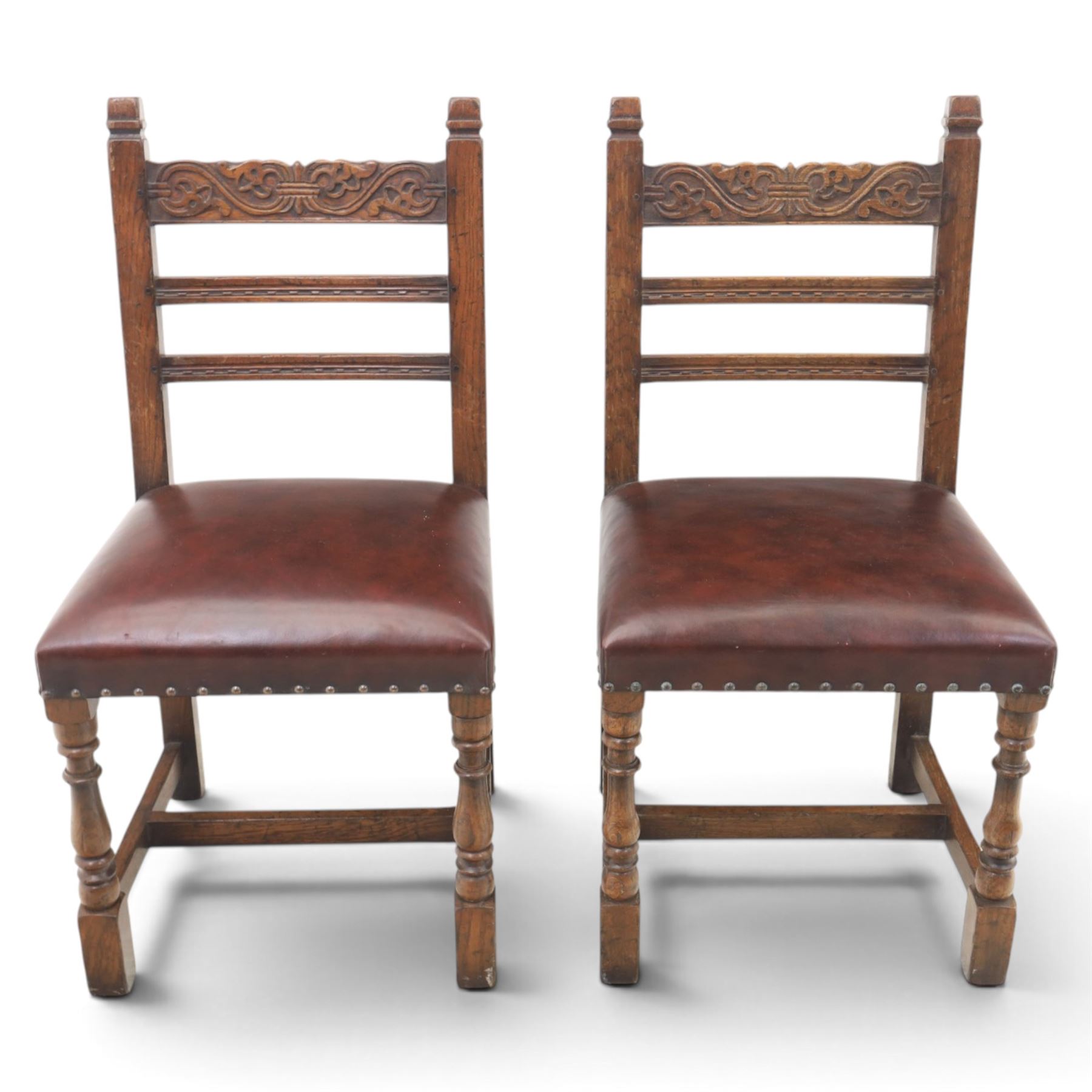 Craftsman made set of four solid oak dining chairs with leather seats, with carved cresting rail, on red leather seats with studded trim, raised on block and turn supports united by H-stretcher