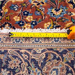 Central Persian Kashan hand-knotted rug,  terracotta field with central shaped ivory and dark blue medallion with palmettes, floral sprays and scrolling vine ornament, with conforming corner spandrels enclosed by a broad navy border of palmettes and flowering vine between multiple guard stripes, with cotton fringe ends 