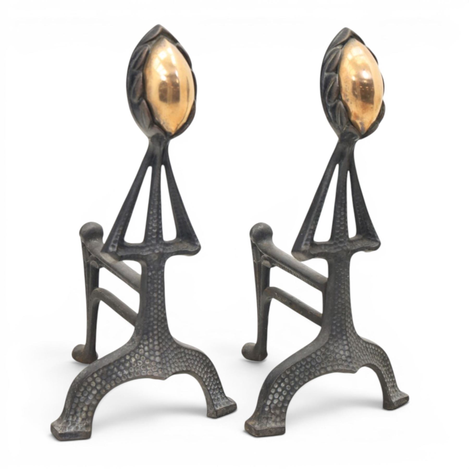 Arts and Crafts cast iron and brass andirons, brass and copper acorn finials above openwork uprights, raised on shaped arched feet with hammered detail