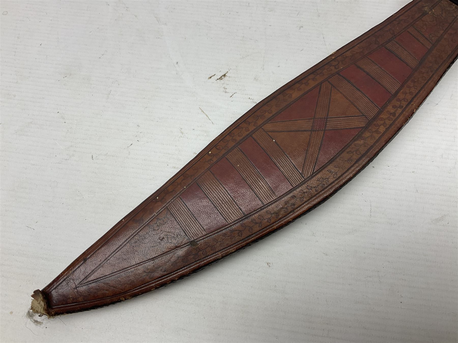 Mandingo sword with 63cm plain curving steel blade and leather covered grip with white metal ribbed spherical pommel; in decorative leather leaf scabbard with plaited tassels and shoulder strap L78cm overall