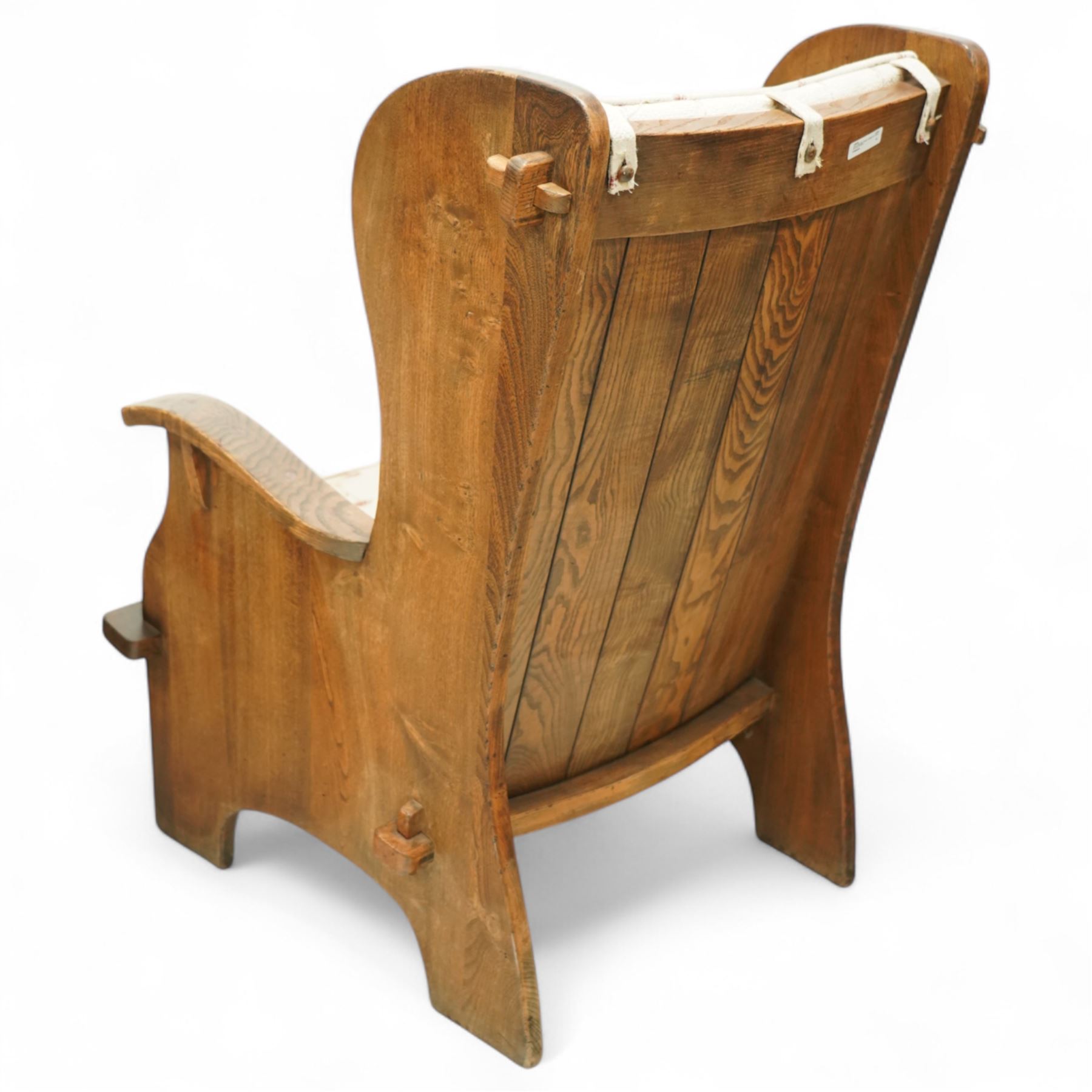 20th century pair of country lambing chairs in light oak, each with high winged back and shaped arms, pegged construction with panelled sides and arched aprons, loose seat and back cushions upholstered in cream floral fabric