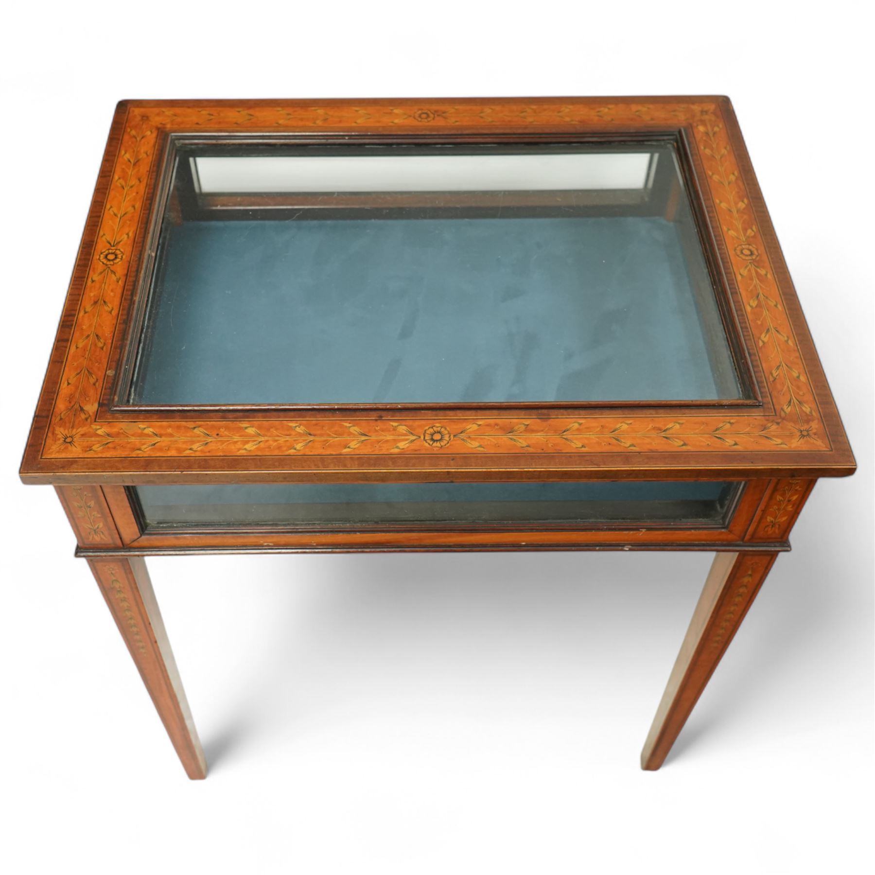 Edwardian satinwood bijouterie table, rectangular glazed top and glazed sides enclosing a blue velvet-lined display well, raised on square tapering legs, decorated throughout with neoclassical foliate inlay