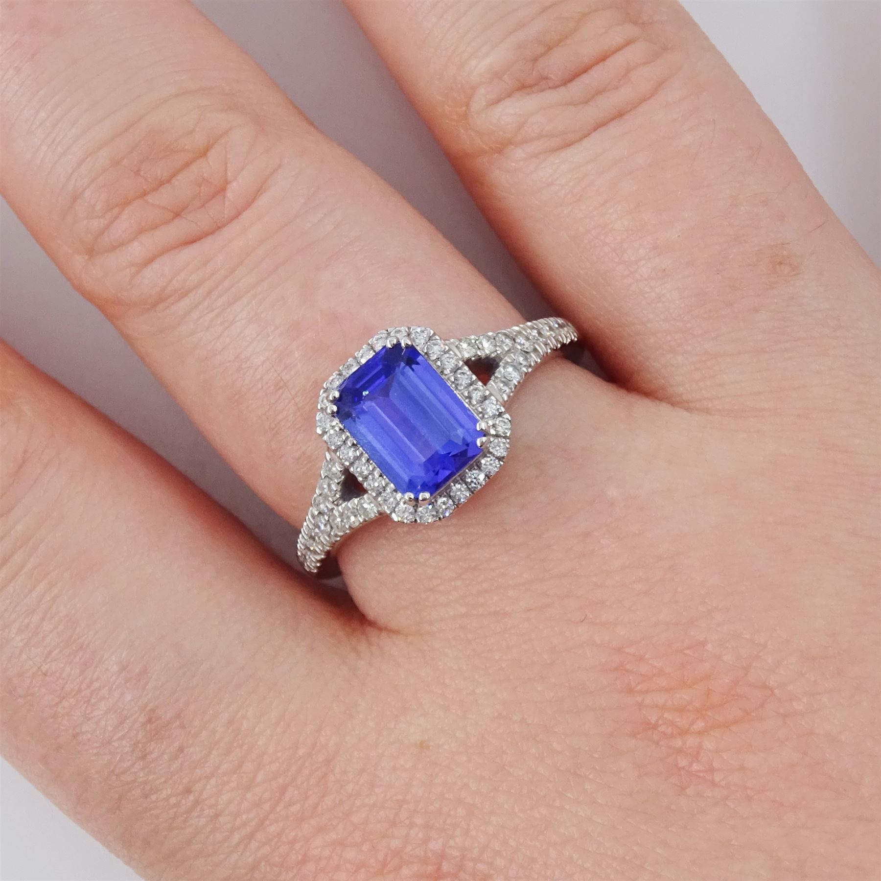 Platinum tanzanite and diamond cluster ring, single emerald cut tanzanite of approx 1.75 carat, with round brilliant cut diamond surround and split diamond set shoulders, signed Rhapsody, hallmarked, total diamond weight approx 0.20 carat