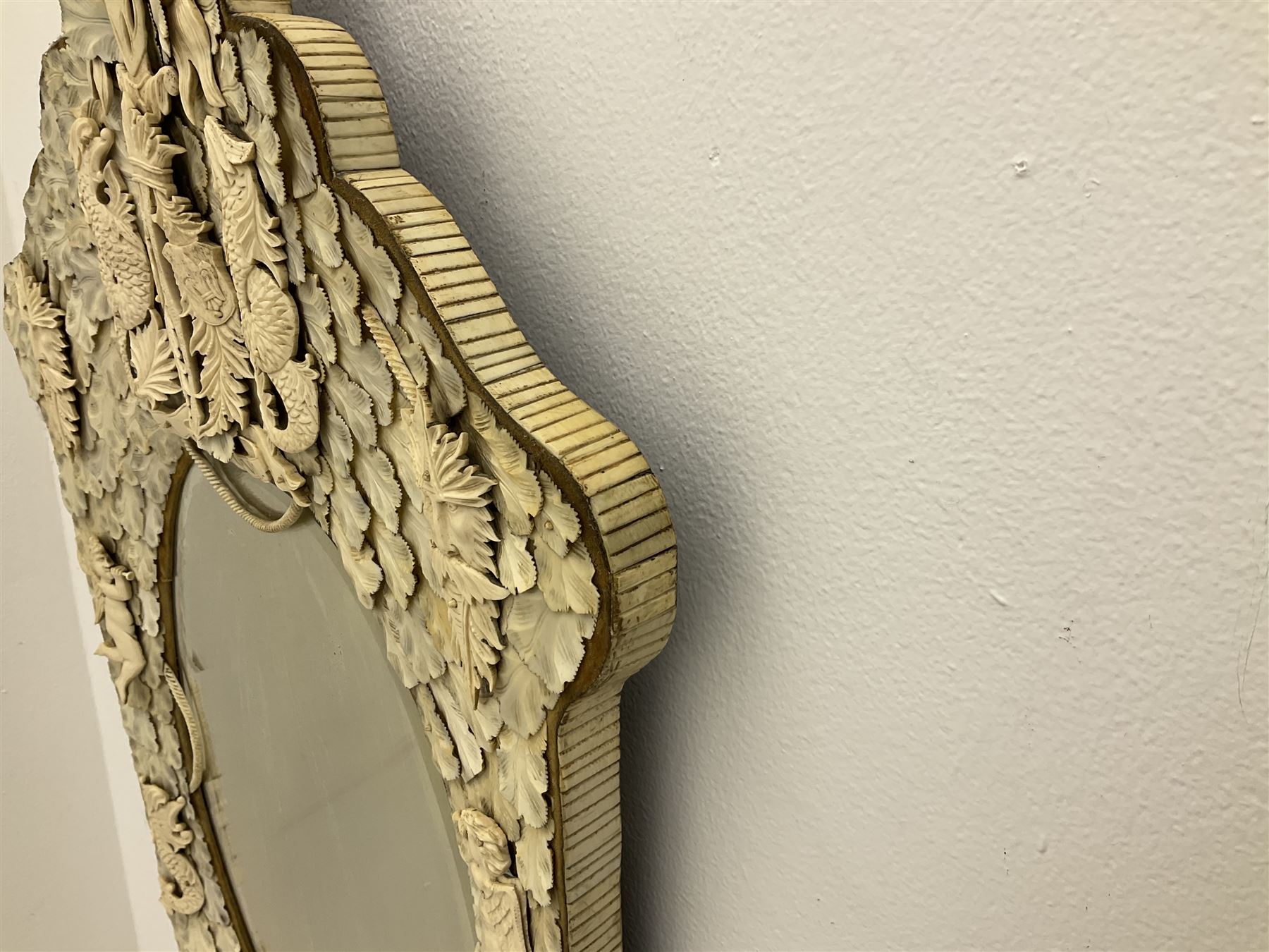 Pair 19th century French Dieppe bone and ivory wall mirrors, the oval bevelled mirror plates within rectangular frames with shaped tops, profusely decorated with ivory leaves, further detailed with carved bone armorial type crest inscribed 'SGOTORVM', putti, fish and mask heads, H81cm W48cm