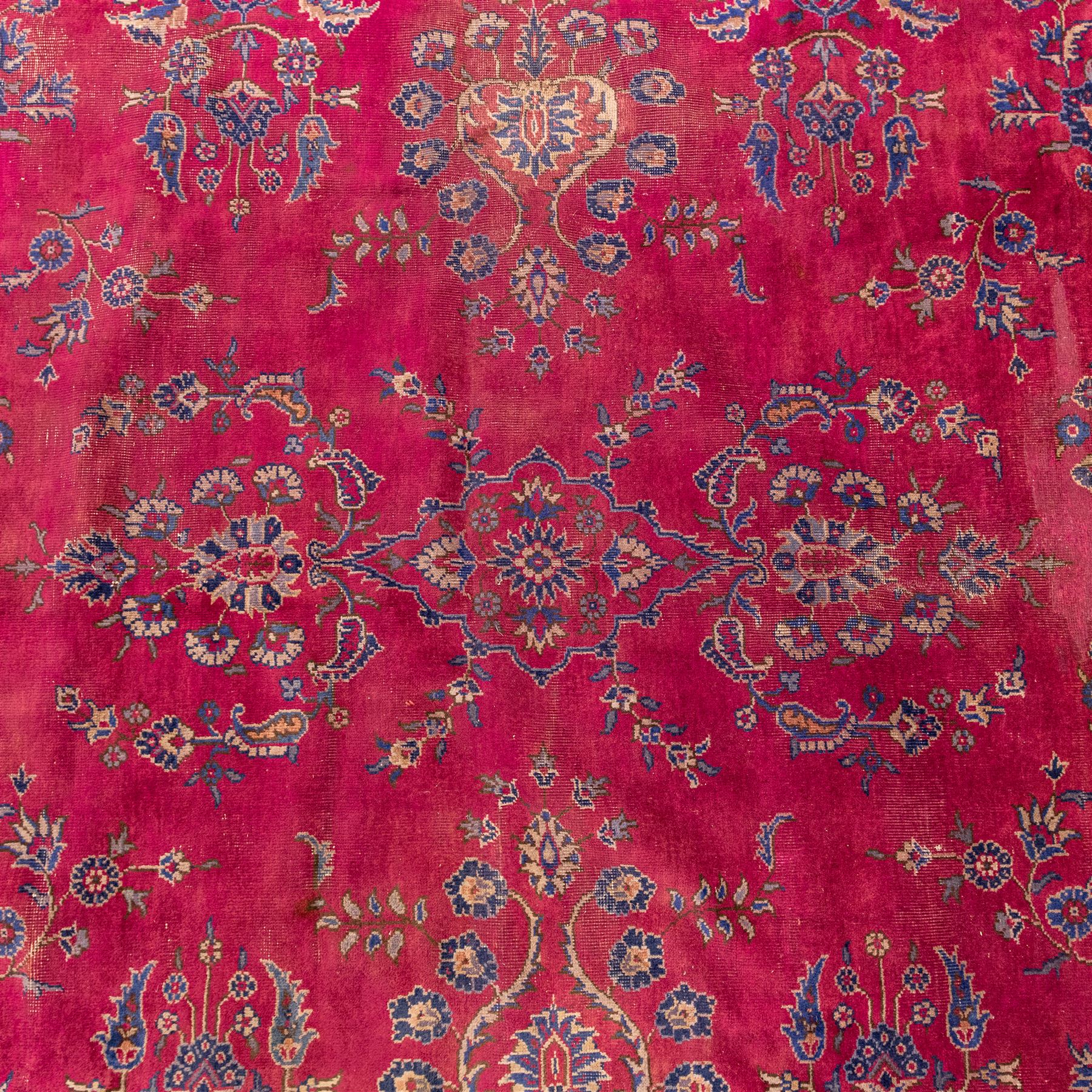 Large Persian-style mahal-type hand-knotted carpet, of rectangular form with a deep crimson field decorated with an all-over arrangement of stylized floral sprays and palmettes, with a central subtle medallion composition enclosed by a dark navy main border of scrolling floral motifs between narrow guard stripes with fringe ends 