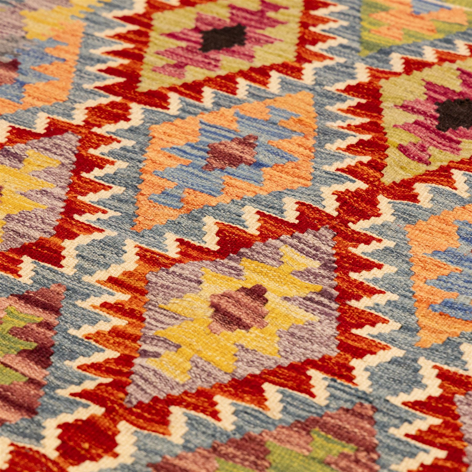 Afghan Chobi flatweave kilim, with a repeating stepped diamond medallion design in ivory, green, rust, teal, purple, indigo, and framed by chevron and geometric borders