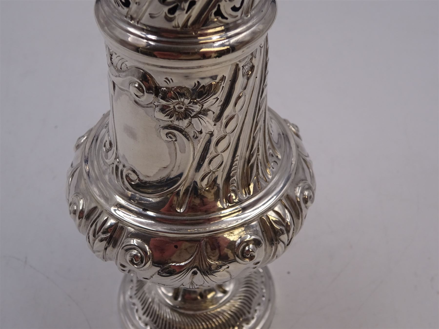 Victorian silver sugar caster, of bellied form, with repousse scroll and foliate decoration, the removable pierced cover with flambeau finial, upon a conforming circular spreading foot, hallmarked Goldsmiths & Silversmiths Co, London 1893, H18.5cm