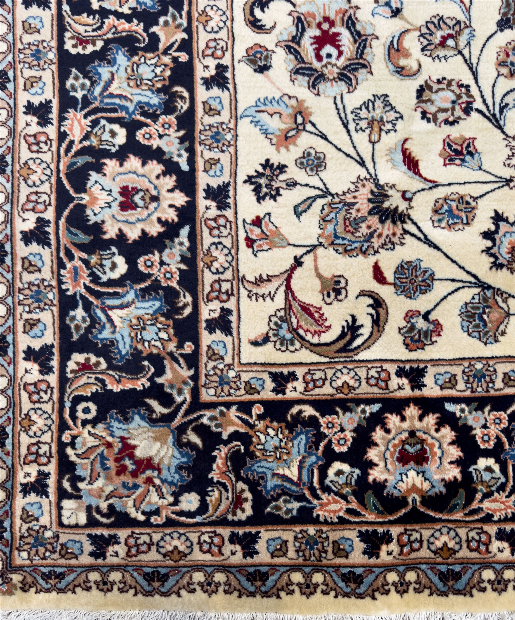 North East Persian Meshed hand-knotted rug, ivory field with scrolling vines, palmettes, and rosettes in shades of blue and brown, within a dark blue border of palmettes and flowerheads between multiple guard stripes, with cotton fringe ends  