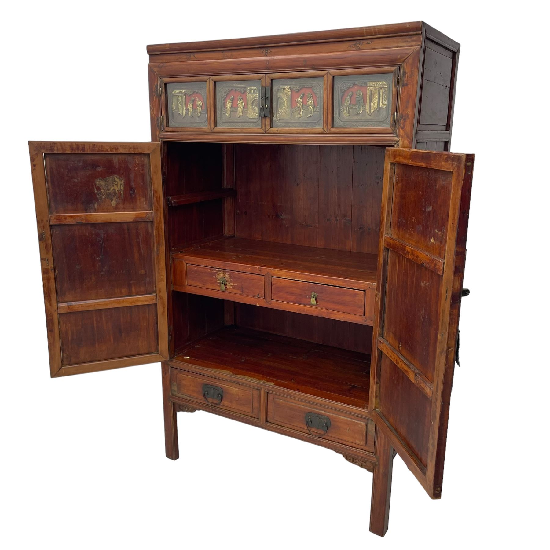 Late 19th century Chinese Qing dynasty red and black lacquered wood cabinet,  Fujianese province, upper cupboard enclosed by two doors with relief carved and gilt panels depicting figures behind glass, the large cupboard enclosed by two panelled doors carved with trailing foliate branches and birds, inscribed with Chinese characters, to the left ‘The red mountains are in the shape of Phoenixes and appear auspicious’ and to the right, ‘Wealth and honour are given by flowers and I hear the sound of the phoenix', fitted with two drawers, on square supports with carved brackets 