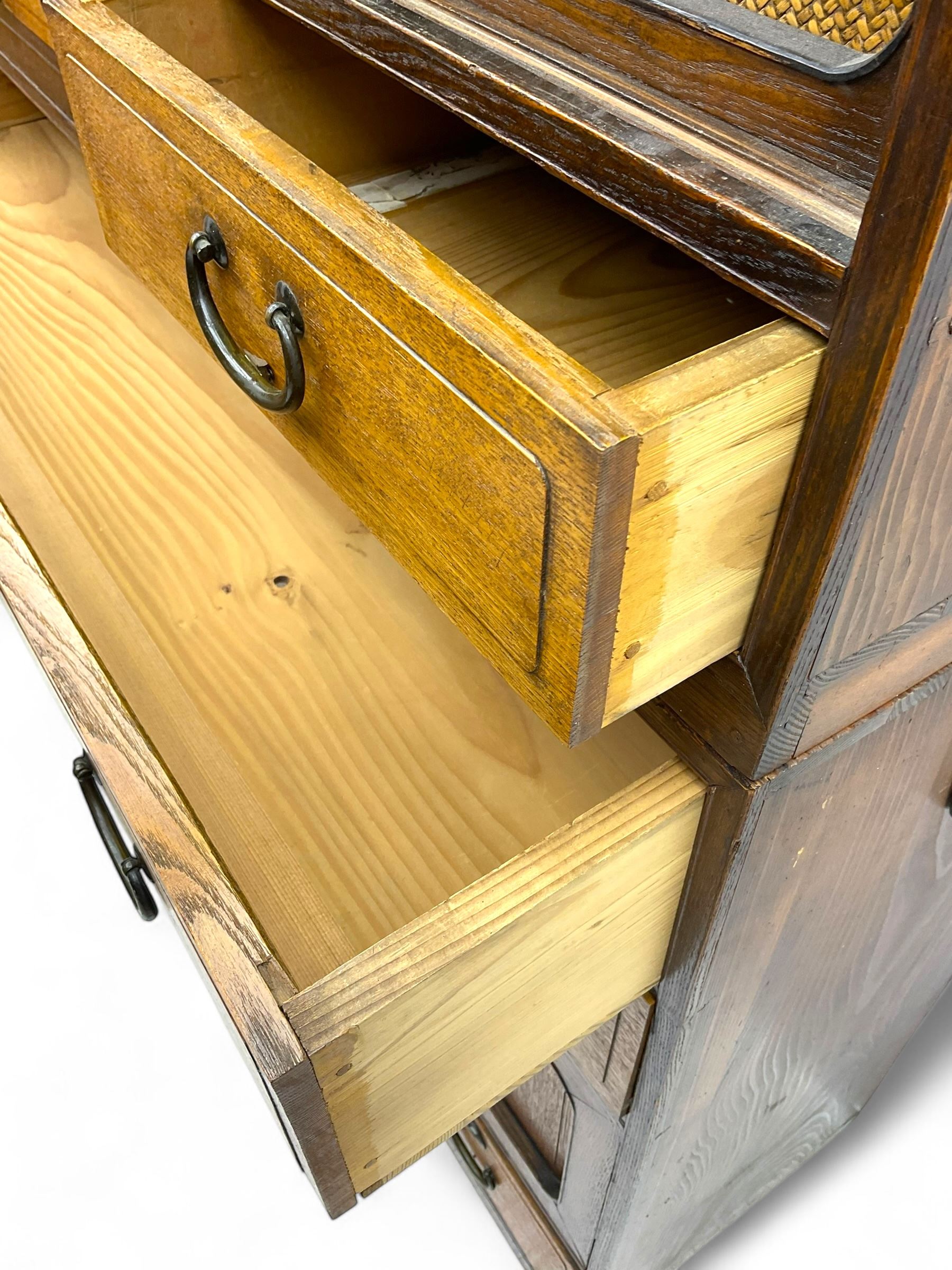 Late Meiji-period Japanese keyaki wood tansu chest, upper section with six sliding woven rattan doors over five drawers, lower section fitted with an asymmetrical arrangement of seven drawers and side cupboard with a hinged door enclosing three additional drawers, iron drop handles to sides