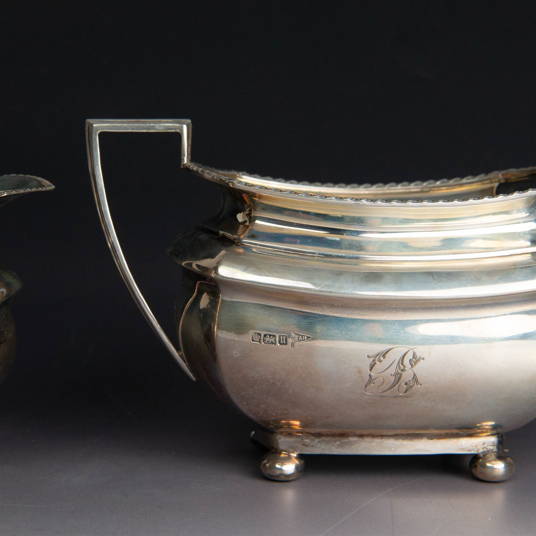 Early 20th century three piece silver tea service, comprising teapot, open sucrier and milk jug, all with oblique gadrooned rim, engraved initial to body and upon four bun feet, the teapot with Bakelite type handle and finial, hallmarked Walker & Hall, Sheffield 1912, contained within an oak presentation case with silk lining