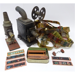  Early 20th century black japanned metal hand cranked projector, embossed ML, with curving chimney H23cm, with a quantity of film strips, and an unmarked paraffin slide projector with forty coloured glass multi-image slides  