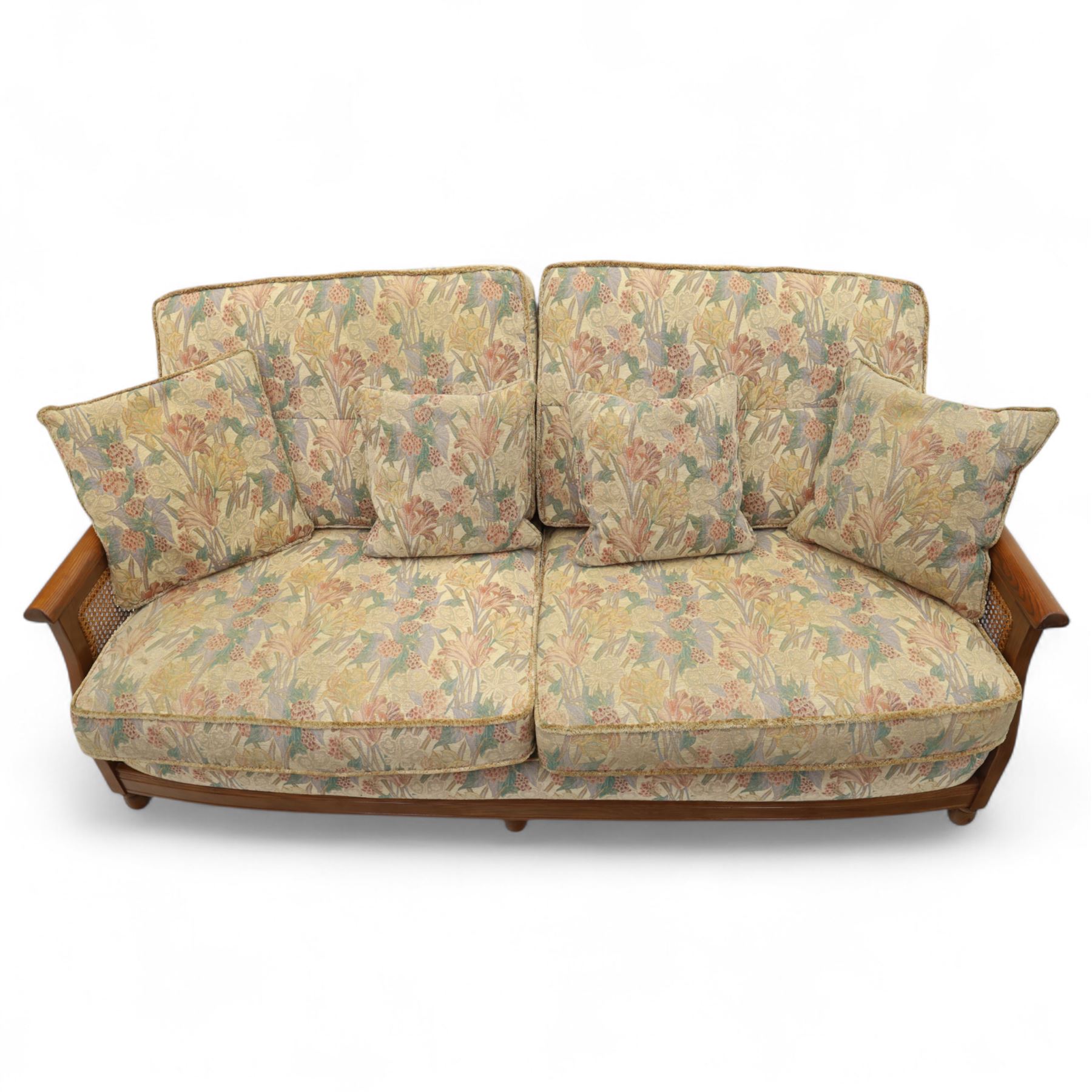 Ercol – bergère four piece suite, including armchair, two seat sofa, three seat sofa and footstool, all with removable floral upholstered cushions, the frames with side caning and rounded arm supports in stained beech

Three seat (H 87cm, D 89cm, W 196cm)
Two seat (H 87cm, D 89cm, W 137cm)
Armchair (H 87cm, D 89cm, W 87cm)
Footstool (H 28cm, D 55cm, W 55cm)