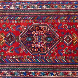 South West Persian Qashqai hand-knotted runner, madder red field  with central vertical succession of stepped lozenge medallions enclosing angular tribal devices and stylized floral motifs, principal medallion in deep indigo with ivory and sky blue highlights, field densely scattered with small geometric ornaments, hooked elements and zoomorphic forms, triangular indigo spandrels enclosed within multiple narrow guard stripes and principal border, with cotton fringe ends 