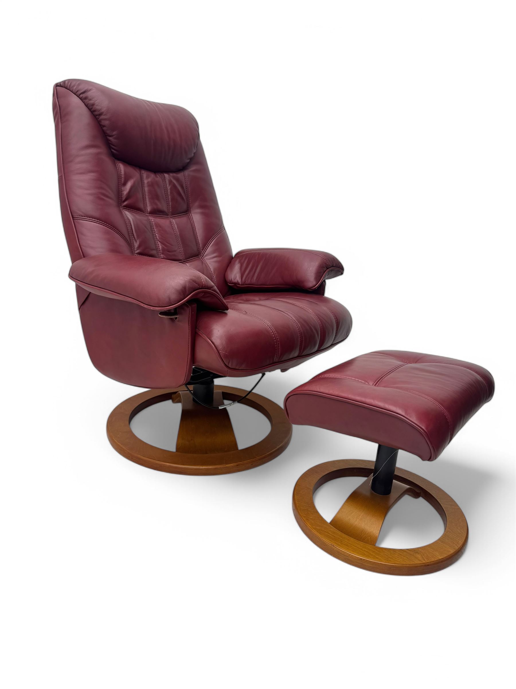 Contemporary burgundy leather reclining armchair and footstool, featuring segmented upholstered cushions and padded armrests, each piece mounted on a circular laminated wood base