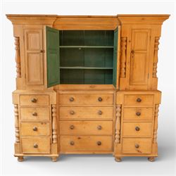 Large Victorian stripped pine reverse breakfront housekeeper’s cupboard, the moulded cornice above a central pair of panelled cupboard doors flanked by single cupboard doors and divided by turned baluster pilasters, the lower section fitted with an arrangement of twelve drawers with knob handles, raised upon bun feet