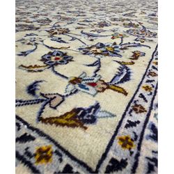 Central Persian Kashan hand-knotted carpet, ivory field with an all-over design of scrolling vines, lotus palmettes, and rosettes in shades of blue, gold, and brown within a blue ground border of palmettes and arabesques between multiple guard stripes