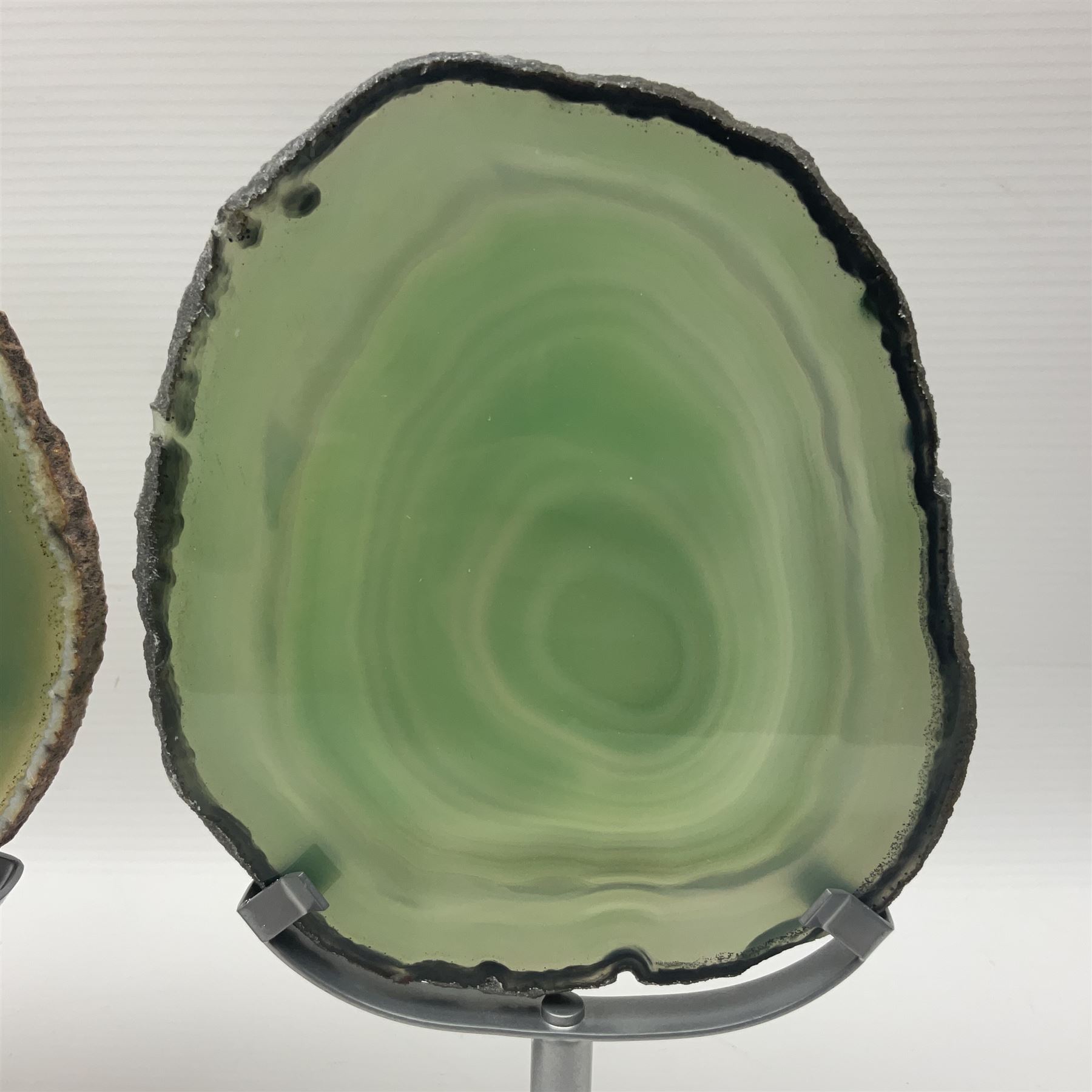 Pair of green agate slices, polished with rough edges raised upon silvered metal stands, H19cm