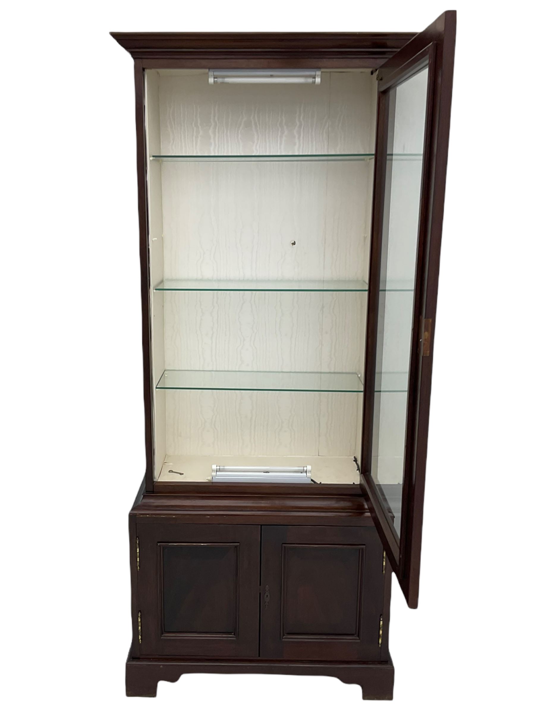 Mahogany display cabinet with hidden compartment, projecting cornice over single glazed door enclosing glass shelves, double panelled cupboard below, the interior with button releasing sliding back compartment, on bracket feet