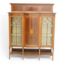 Maple & Co. Edwardian inlaid mahogany display cabinet, raised triple panelled back inlaid with quarter-matched veneers, break bow-fronted top over figured frieze with checkered stringing, enclosed by two astragal glazed doors and central panelled door, oval fan inlay with ribbon tie and trailing bell flowers, on square tapering supports with spade feet united by under tier, with 'Maple & Co.' circular makers plaque to the back