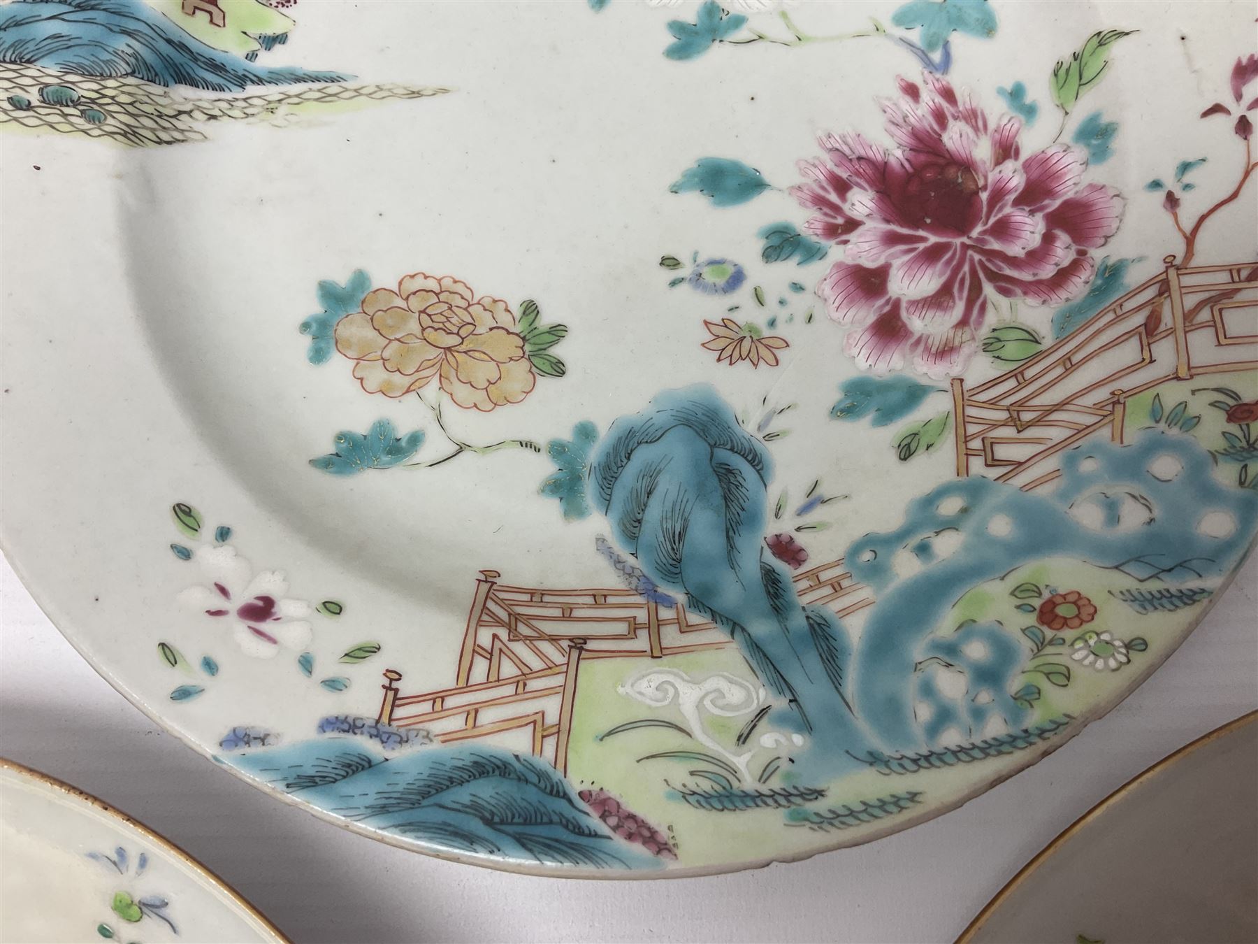 Three 18th century Chinese Famille Rose plates, the first example enamelled with blossoming peonies, rockwork and fence, the other two examples of similar design, decorated with blossoming peonies and sprigs within shaped inner borders, each approximately D23cm