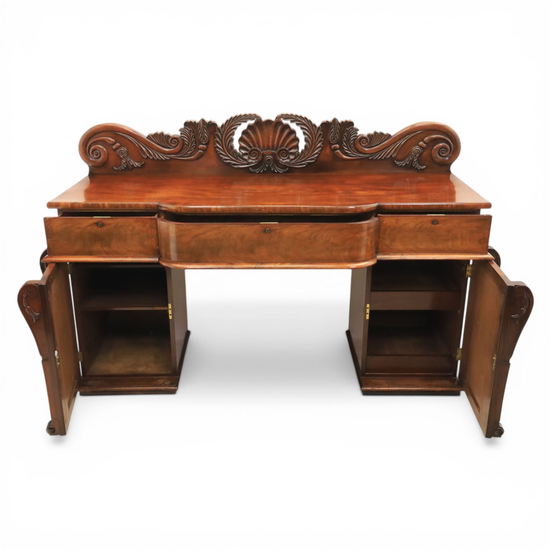 Mid Victorian mahogany pedestal sideboard, the rectangular top with raised back centred by a carved shell within scrolling acanthus and foliate cresting, over a central shaped frieze drawer flanked by two short drawers, above a kneehole recess, flanked by panelled cupboard doors with carved corbel supports, enclosing shelved interiors