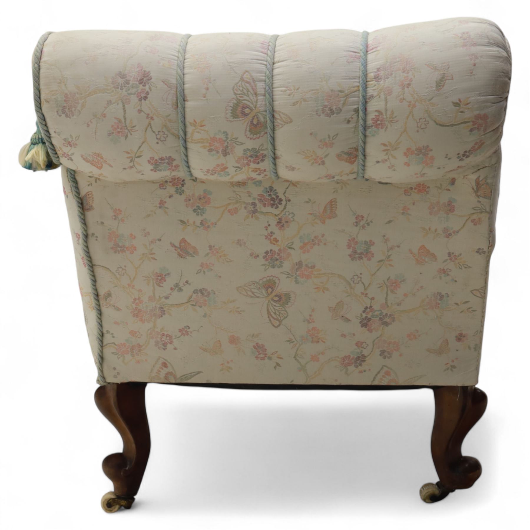 Late 19th century upholstered chaise longue, the gently scrolled headrest above a buttoned back and sprung seat, upholstered in a floral patterned fabric, raised on cabriole mahogany supports with ceramic castors