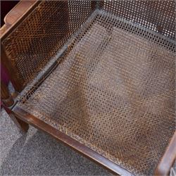 Pair of early 20th-century mahogany Bergère armchairs in the manner of Gillows, the back and seat with woven cane panels with loose red velvet cushions, the frame with swept arms with tapered and reeded uprights, raised on tapered square-section front legs terminating in brass cup castors 
