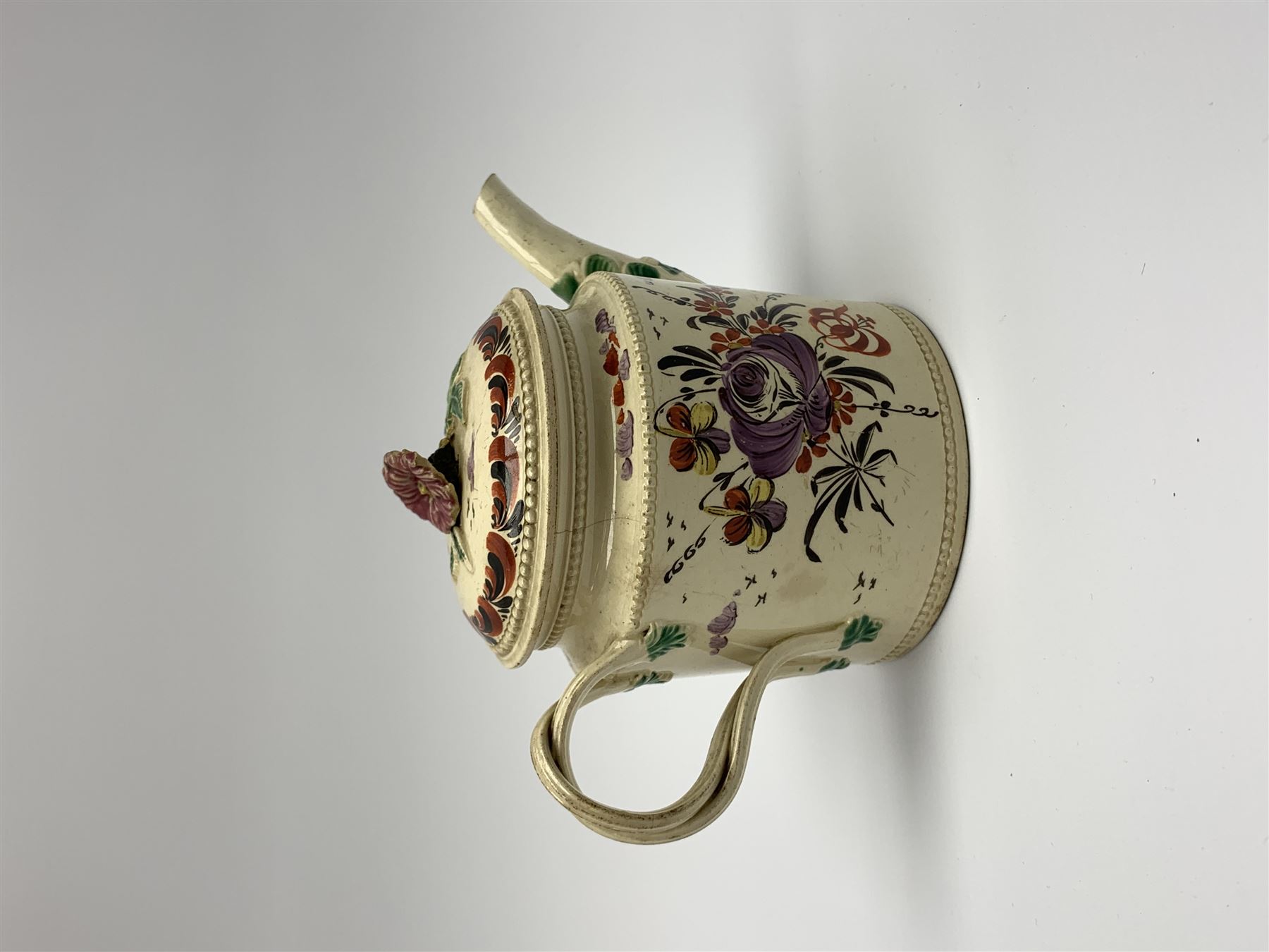 18th century creamware teapot, probably Leeds, with reeded entwined handle and floral finial to the cover, the body with hand painted polychrome decoration of figure to one side, and floral spray to the other, collectors paper label beneath inscribed Leeds Pottery, H11.5cm