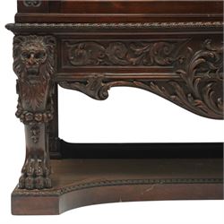 Large and impressive 19th century heavily carved mahogany display cabinet, the ornate pediment carved with a central scalloped and foliate rocaille motif with extending acanthus leaves and egg-and-dart moulding flanked by acanthi finials, over a central cartouche with carved bow-and-arrow motif and trailing scrollwork, the bookcase enclosed by two glazed doors with bevelled glass sides, the base with a gadrooned upper edge over a central rocaille ornament with scrolling acanthus leaves, the panelled frieze with further foliate motifs, raised on large carved snarling lion mask supports with floral garlands and claw feet, united by a concave rectangular platform base with gadrooning egg-and-dart moulding