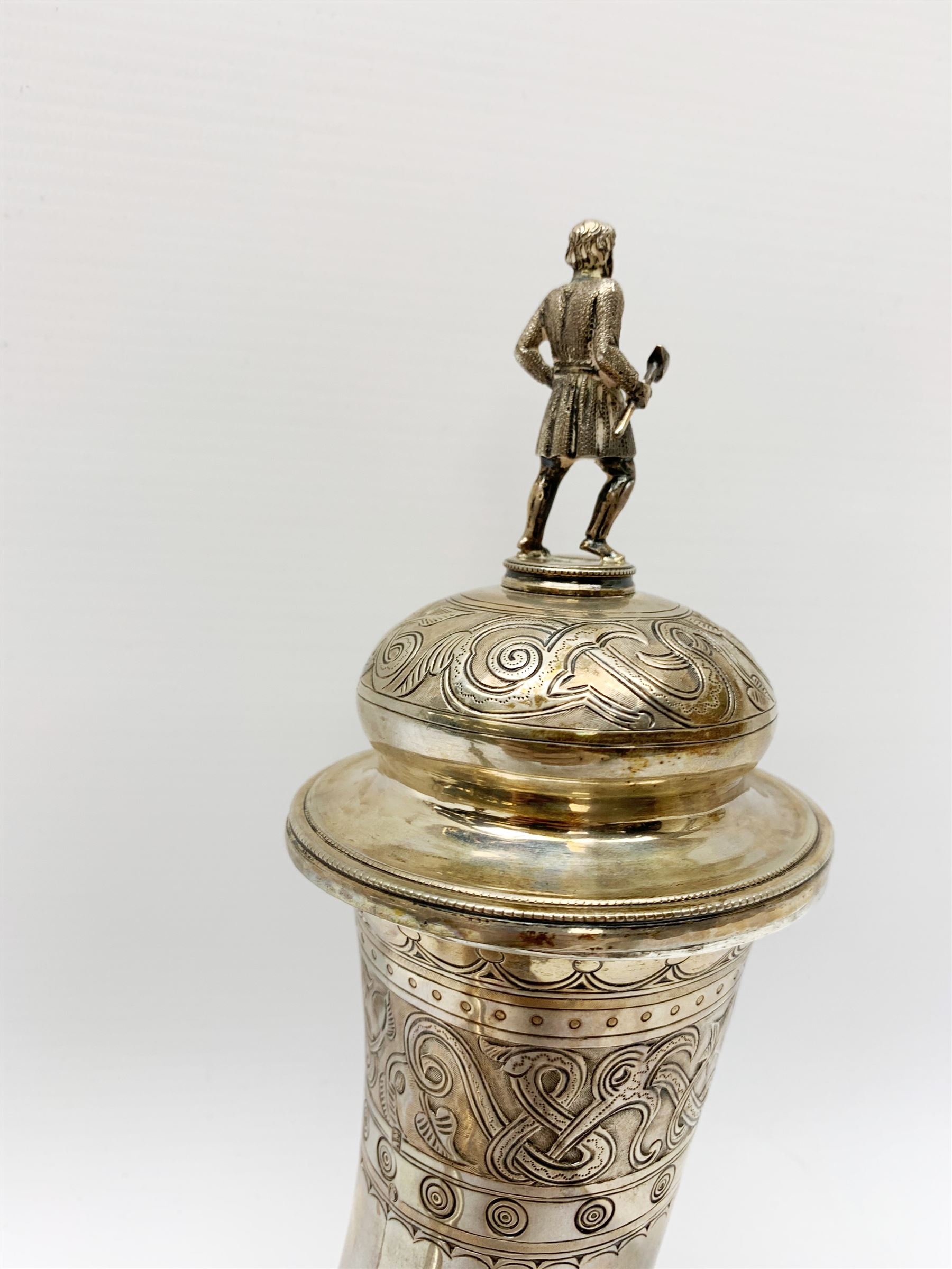 Late 19th century Danish silver drinking horn and cover, the body with hexagonal and beaded finial, raised upon two talon feet and further scroll foot, chased with scrolling foliate and zoomorphic bands, the detachable domed cover with conforming decoration surmounted by a figure holding a hammer, the cover interior impressed with maker's mark (partly worn and indistinct), alongside Danish Three Towers mark for 1881, with the Assay Master mark for Simon Groth (1863-1904), H23.5cm, weight 14.75 ozt (459 grams)


