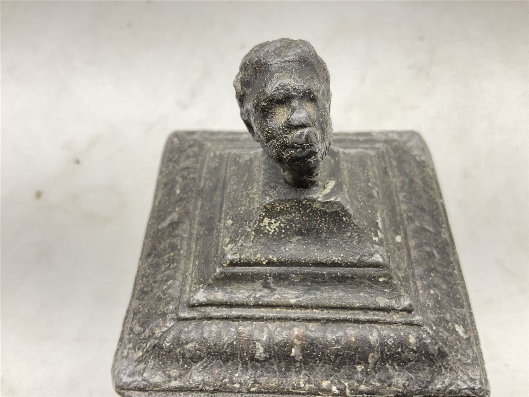 19th century lead tobacco box, the body of square form decorated with panels of courting couples in relief supporting stepped tapering lid with figural male head finial, H18.5cm