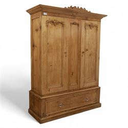 Late 19th century pine wardrobe, with stepped cornice over triple panelled doors, applied foliate carvings to outer panels, raised over a separate pine plinth drawer with moulded facia and twin glass pulls
