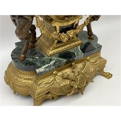 20th century continental gilt metal Lyre mantle clock on a raised plinth with paw feet and variegated green marble base, with two bronzed metal figures of mythological cherubs with animal legs and cloven hooves holding a festooned garland swag, surmounted by a marble urn and finial, eight-day twin barrel Hermle striking movement with a floating lever balance, striking the hours and half-hours on two bells, white enamel dial with roman numerals, minute track and serpentine steel hands, with a cast brass bezel and bevelled convex glass, dial inscribed “Imperial”.


