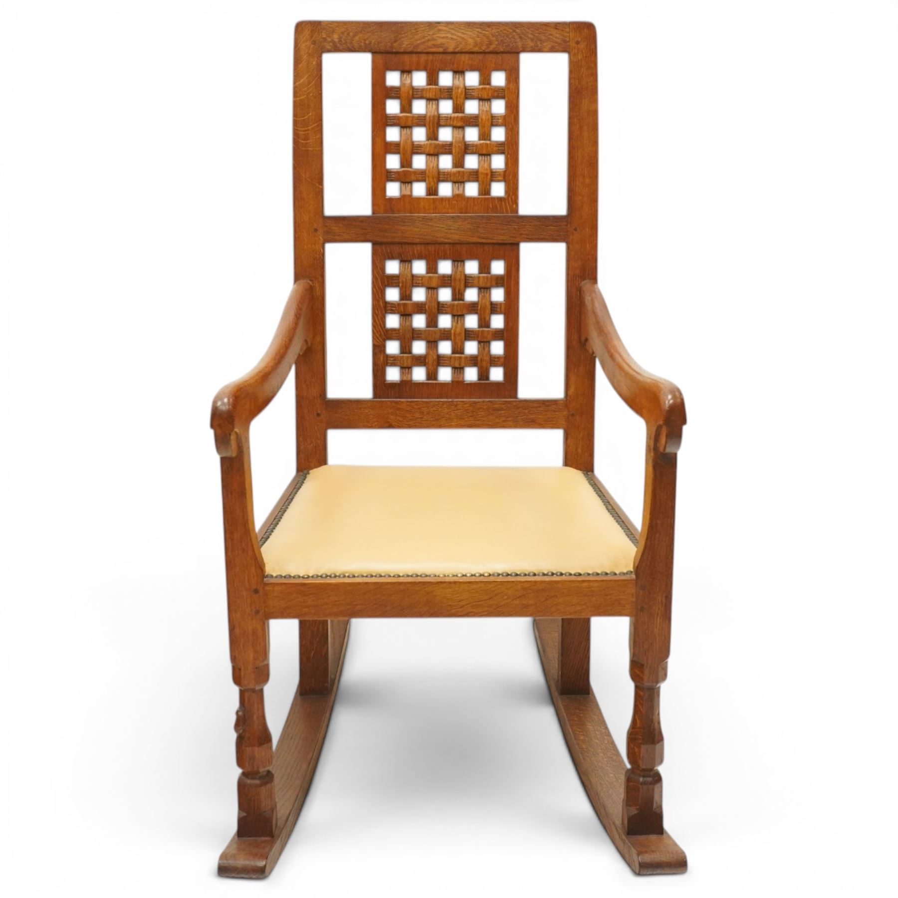 Mouseman - 1940's dark-honey oak rocking chair, high back with pierced double-lattice panel, over a beige-leather upholstered seat, shaped arm terminals above turned octagonal front-supports united by rocker base, with carved mouse signature, by the workshop of Robert Thompson of Kilburn
