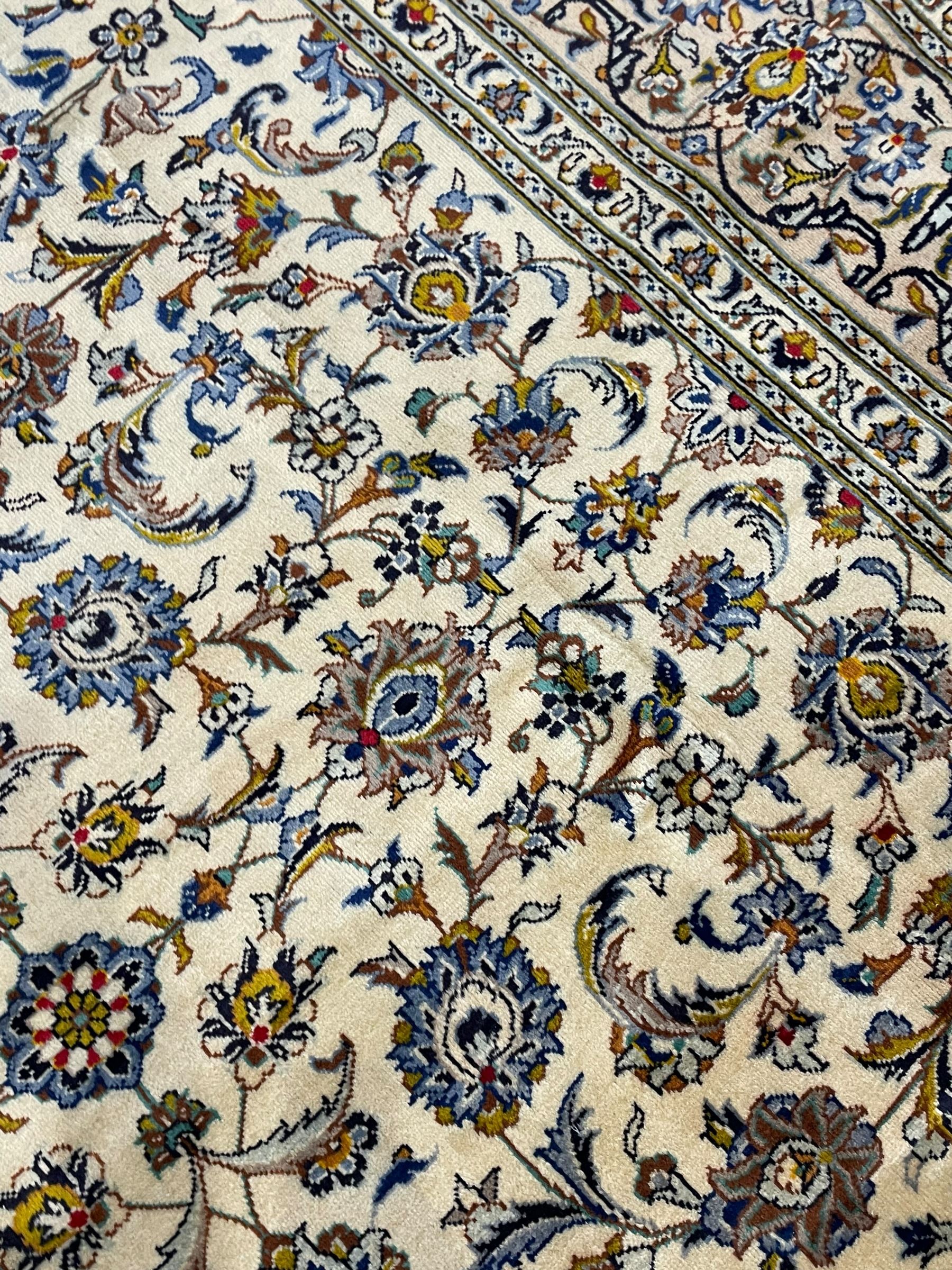 Persian Kashan Ivory ground carpet, the busy field decorated all over palmettes and trailing branches, scrolling border interspersed with stylised plant motifs, within guard stripes