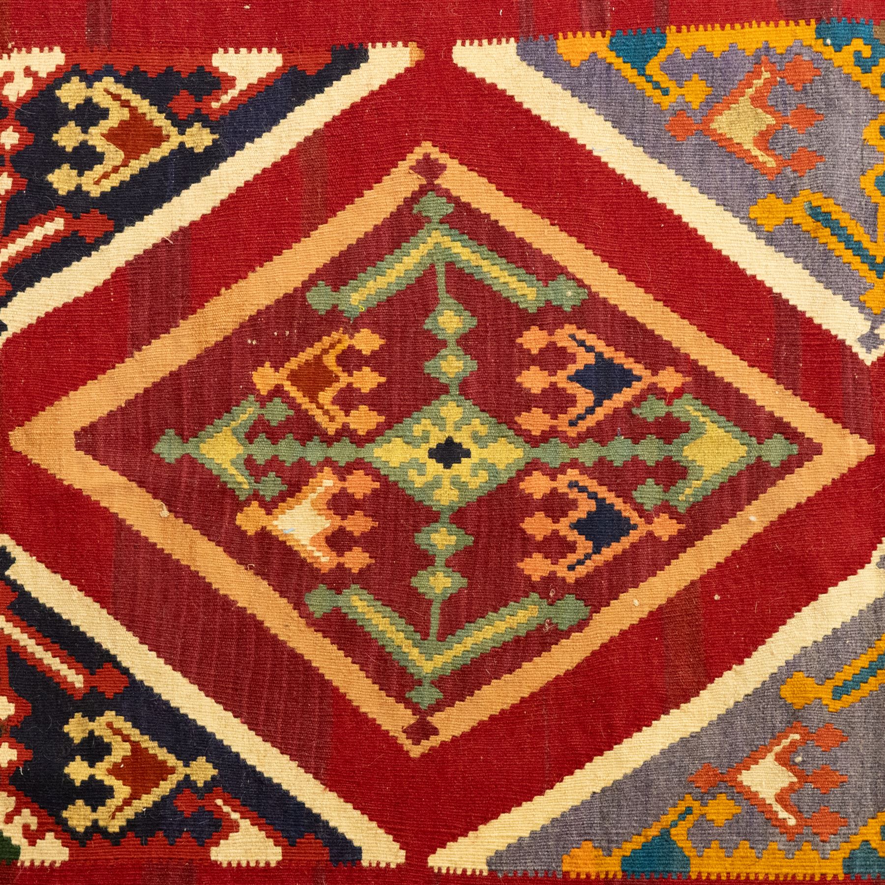 South West Persian Qashqai flatweave kilim, madder red ground with stacked diamond panels filled with latch hook and angular floral motifs, enclosed by multiple geometric borders in palettes of indigo, green, and ochre 