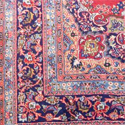 North East Persian Meshed hand-knotted rug, madder red field with central multi-lobbed medallion in shades of indigo, ivory, and sofa pastel tones surrounded by scrolling floral vines, palmettes, stylized blossoms, floral sprays, and cartouches, framed by Indigo spandrels, enclosed within a broad dark blue main border, flanked by multiple narrow guard stripes, with fringe ends 