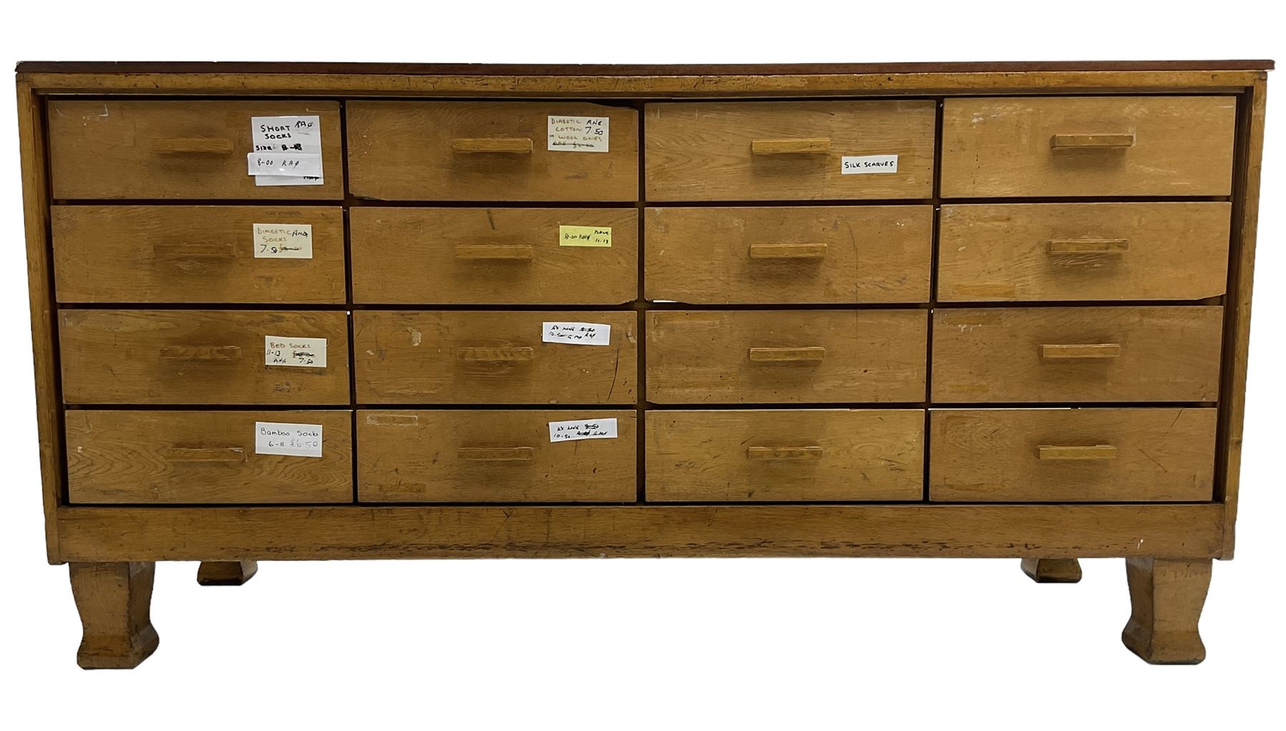 Early 20th century oak framed haberdashery shop counter, veneered top with glazed front and sides, fitted with sixteen graduating drawers with oak fronts and handles, raised on shaped supports