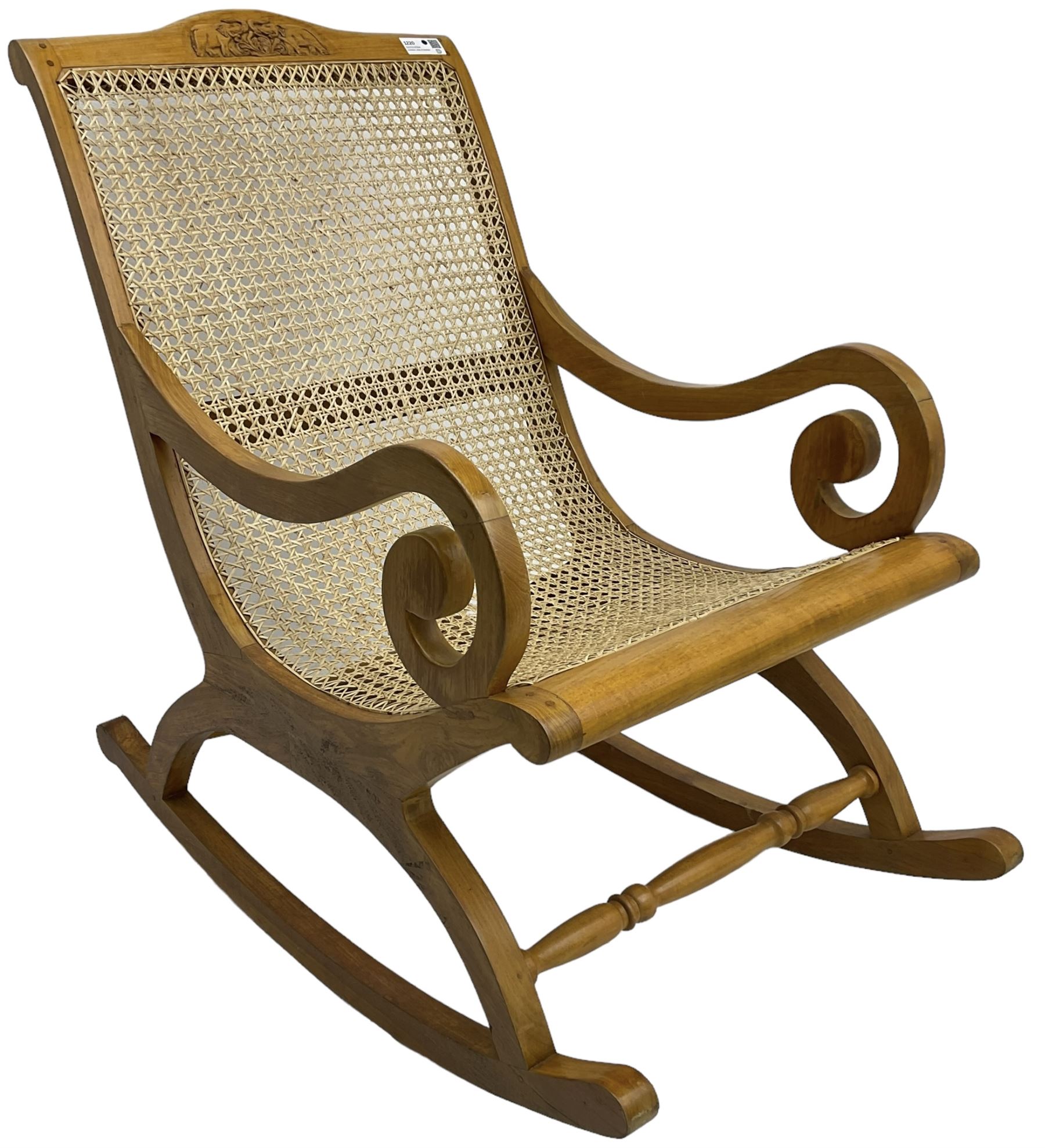 Late 20th century teak framed plantation style rocking chair, cresting rail carved with two elephants with upraised trunks, cane back and seat with scrolled arm terminals, rocker base united by turned stretcher