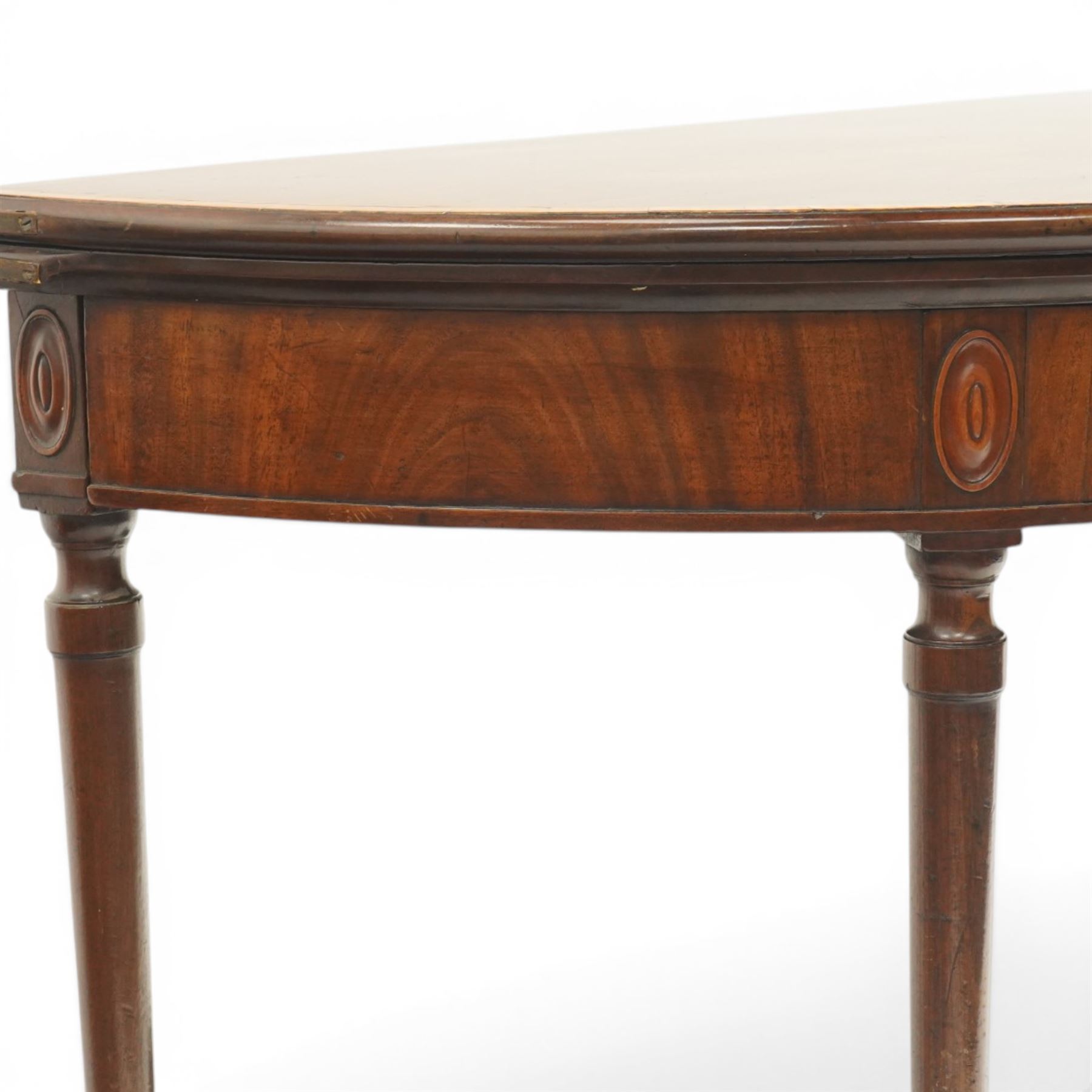 Georgian mahogany demi-lune card table, the lunette shaped top with cross-banded and boxwood-strung edge, opening to reveal baize-lined interior and supported by rear gatelegs, over a banded frieze with applied oval plaques, raised on turned and tapering supports