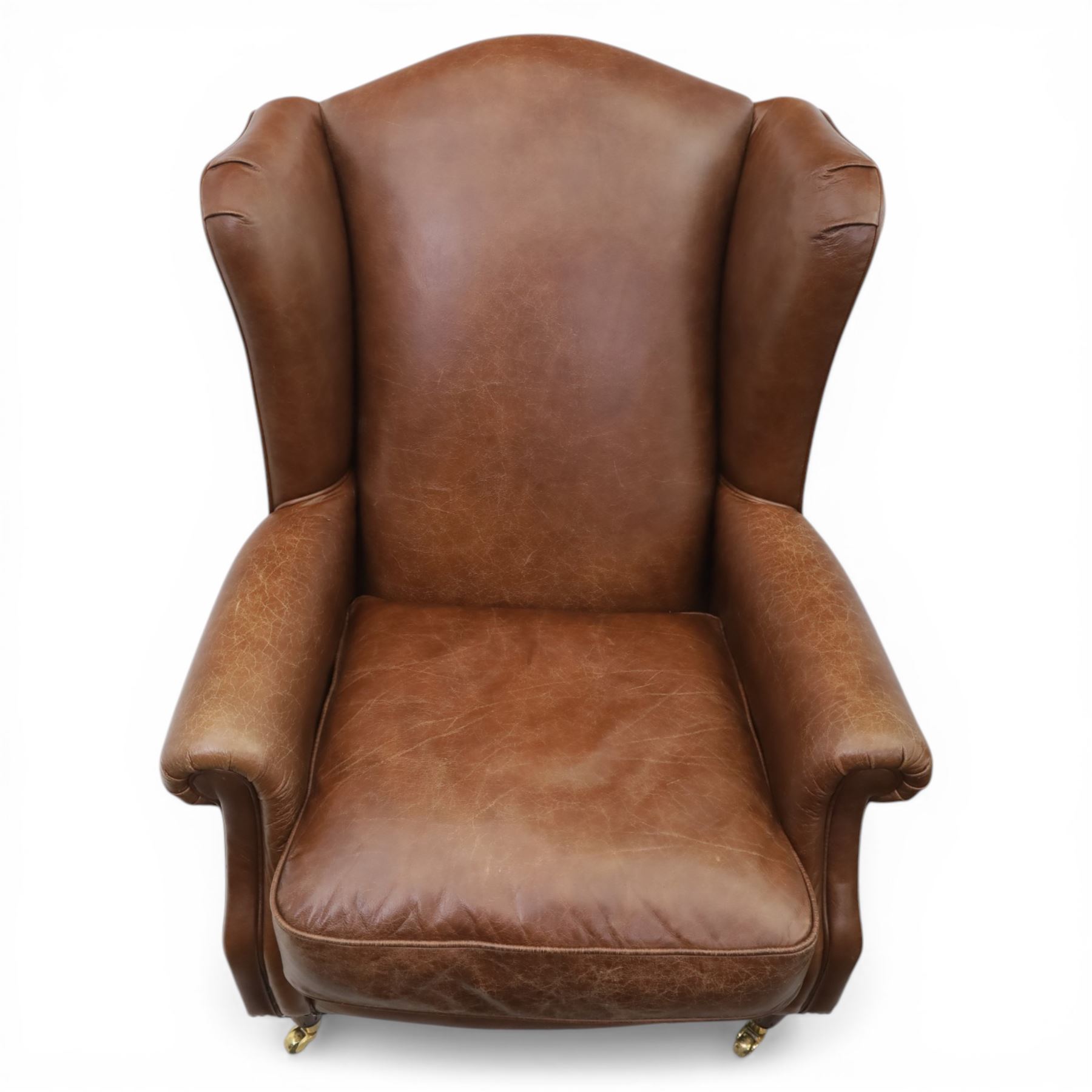 Laura Ashley - Pair of brown leather wingback armchairs, with scrolled arms and loose cushion seat, brass studded trim, on cylindrical tapering legs terminating in castors