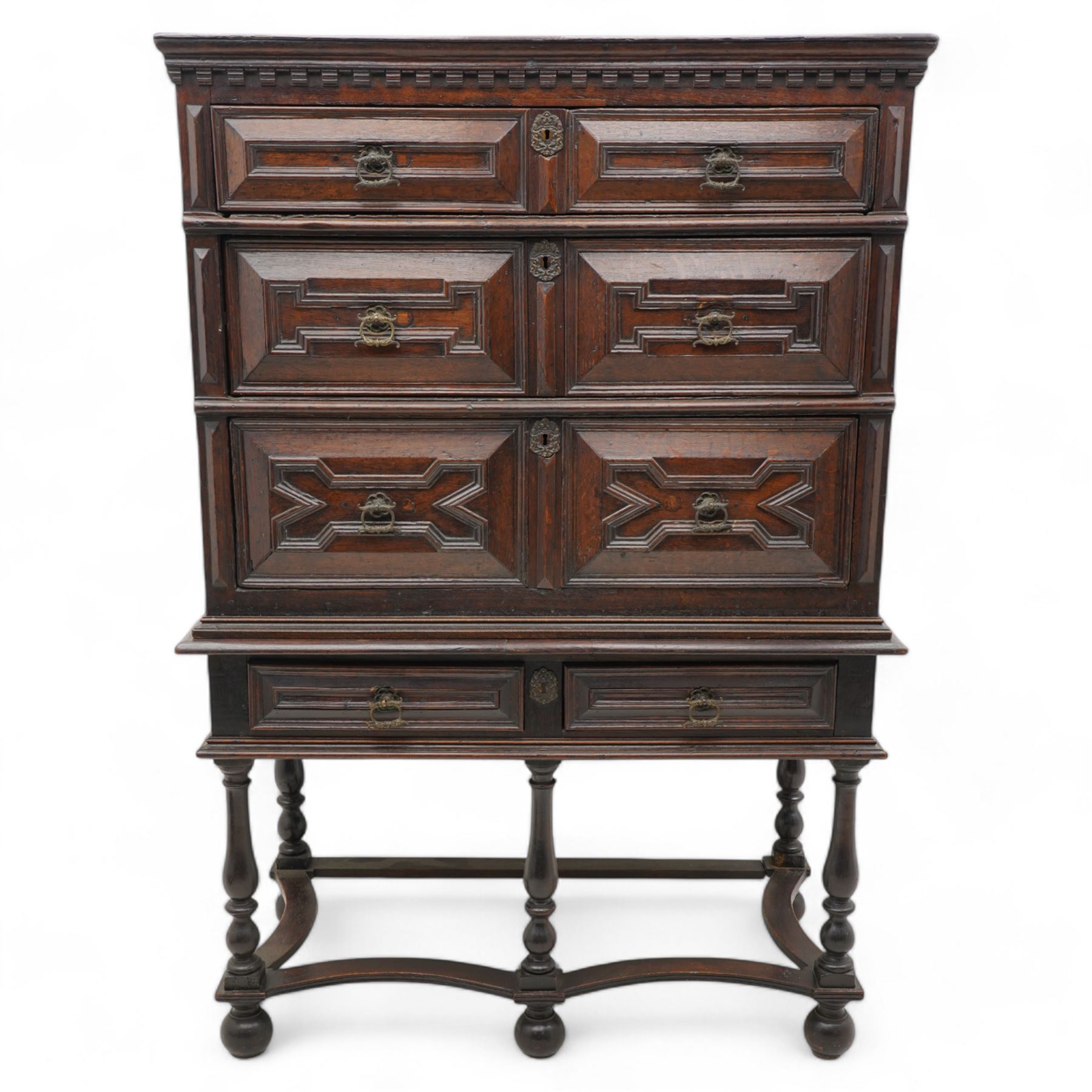 17th century oak chest on stand, moulded cornice over block work frieze, the upper section fitted with three long drawers each decorated with applied geometric mouldings and faceted panels, panelled sides with moulded frame, the stand fitted with two drawers, on five turned supports united by plan flat stretchers, terminating to turned feet