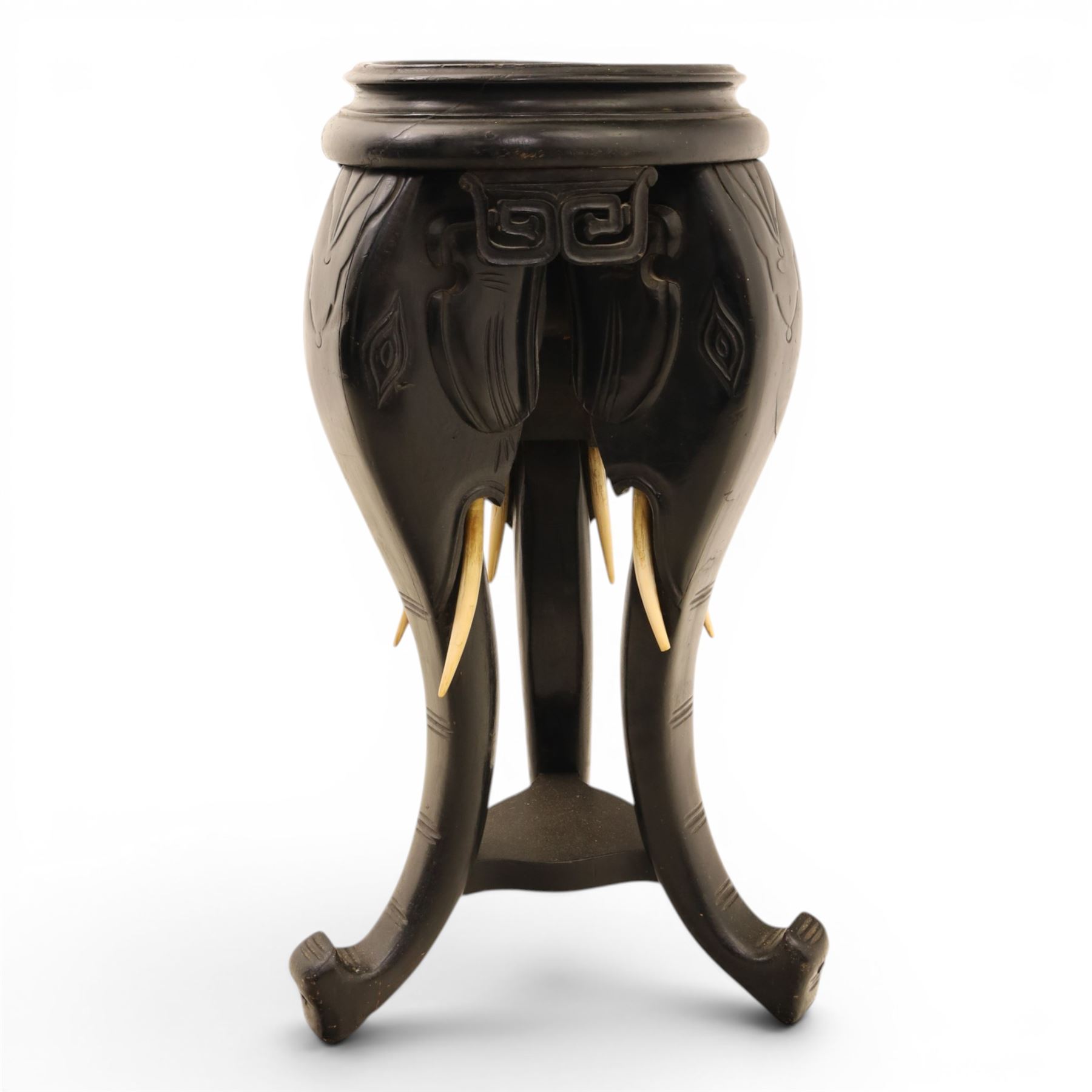 Oriental design black lacquered jardinière stand, circular moulded top with raised rim, the base formed as three elephant heads with carved ears and simulated tusks, on shaped supports with paw terminals