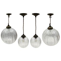 Set of two small and two large pendant lights, each with clear glass spherical shade with moulded swirl pattern, suspended from twisted cords, brass ceiling rose