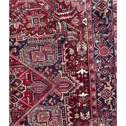 Northwestern Persian Heriz carpet, the madder red field centred by a large octofoil medallion with serrated edge, flanked by ivory stepped spandrels and geometric floral motifs in indigo, ochre and sky blue, enclosed by a navy border of rosettes and angular vines, from the region of Heriz