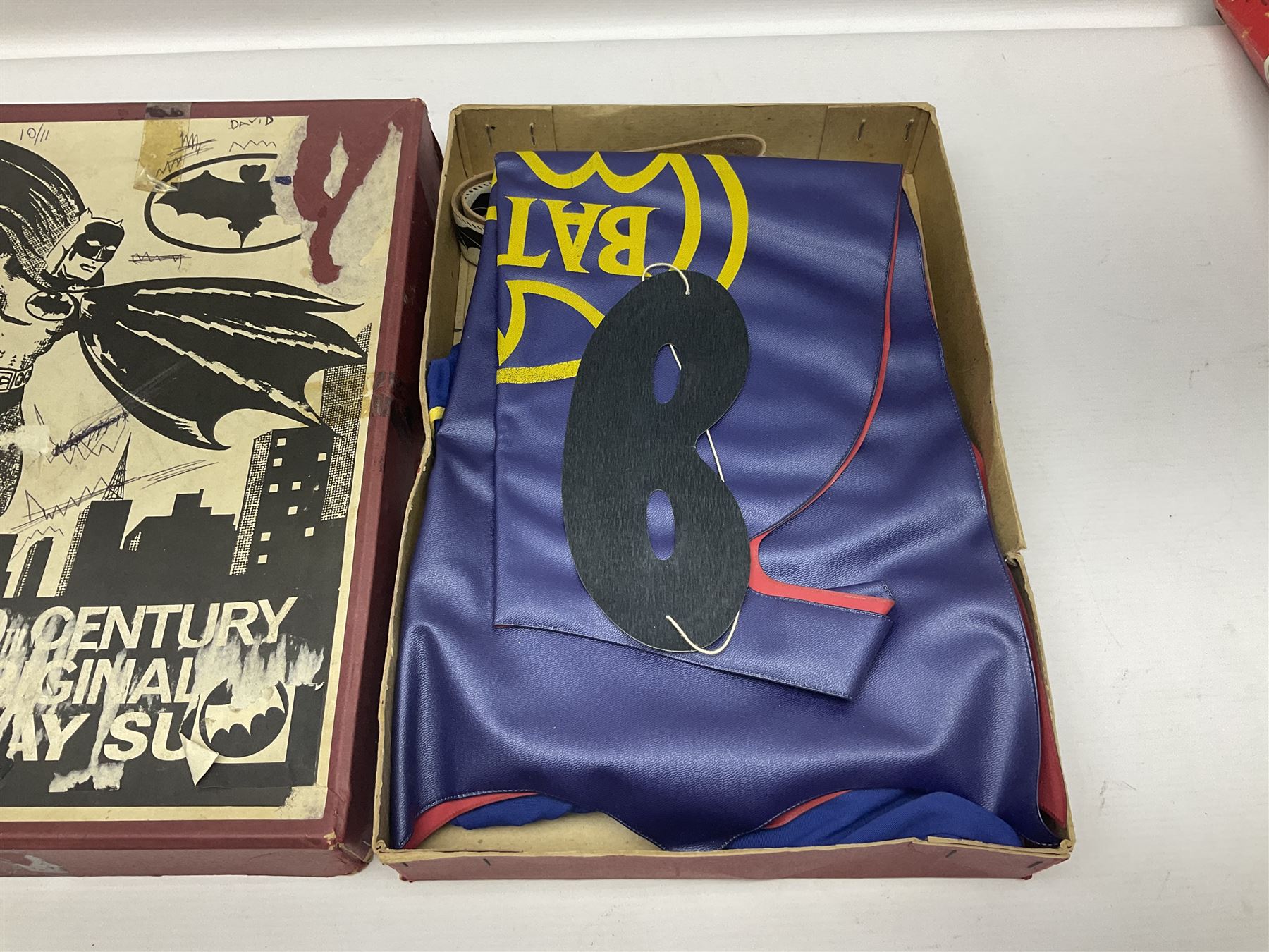 Two Boxed Batman Playsuit Costumes - 1960s 20th Century Original Play Suit, black eye mask, plastic vinyl cape/gauntlets, leather style belt, blue/yellow shirt, with Bat motif and blue/yellow pants; in original illustrated lidded box; and 1976 Decker Batman Playsuit costume, vinyl cape/ mask/gloves/boot tops/yellow belt, grey cloth top and pants; in original illustrated box (2)
