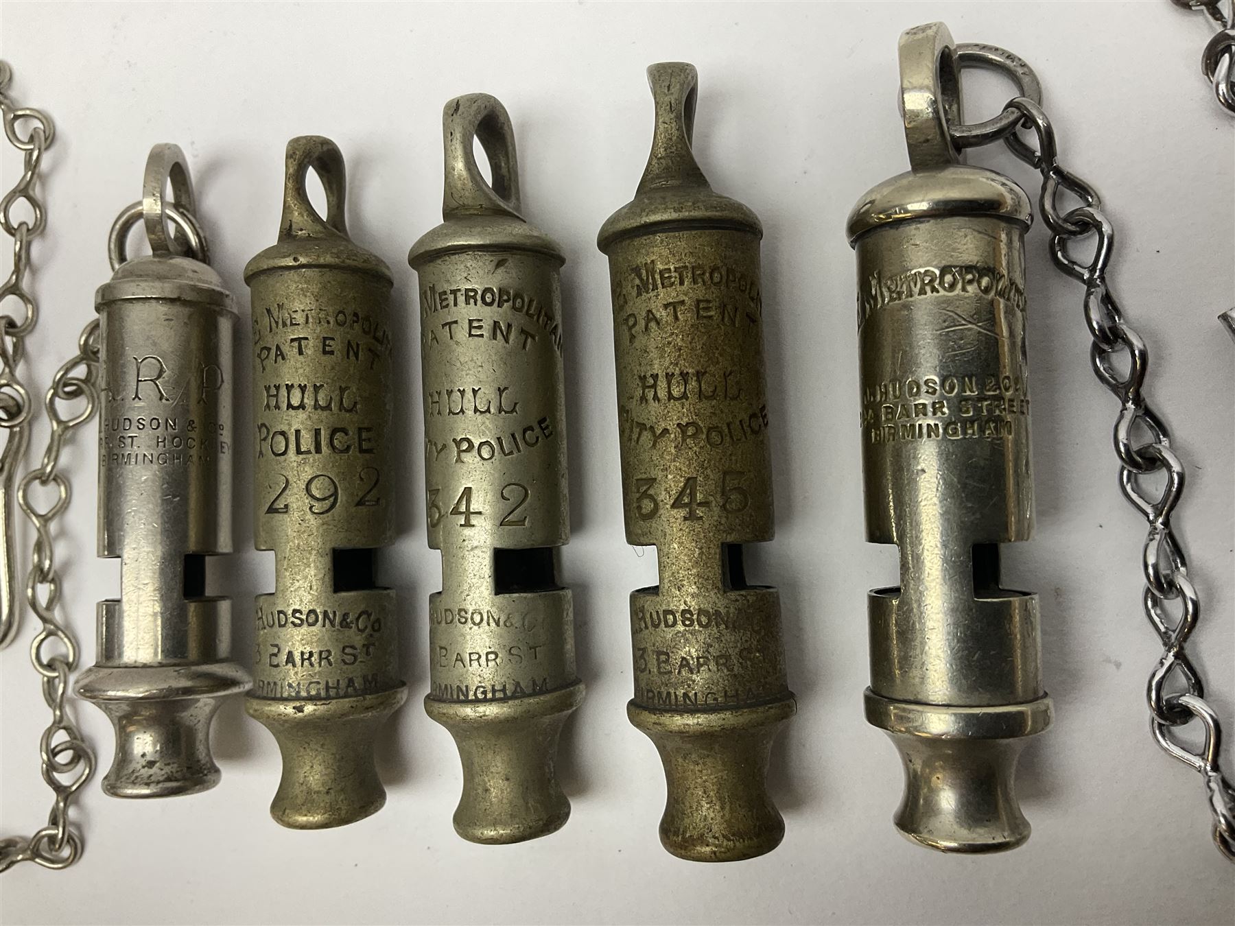 Three Hull City Police 'Metropolitan' whistles by J. Hudson 13 Barr Street Birminham, each with impressed collar number; another 'Metropolitan' police whistle with chain; and an ARP whistle by Hudson & Co with chain (5)